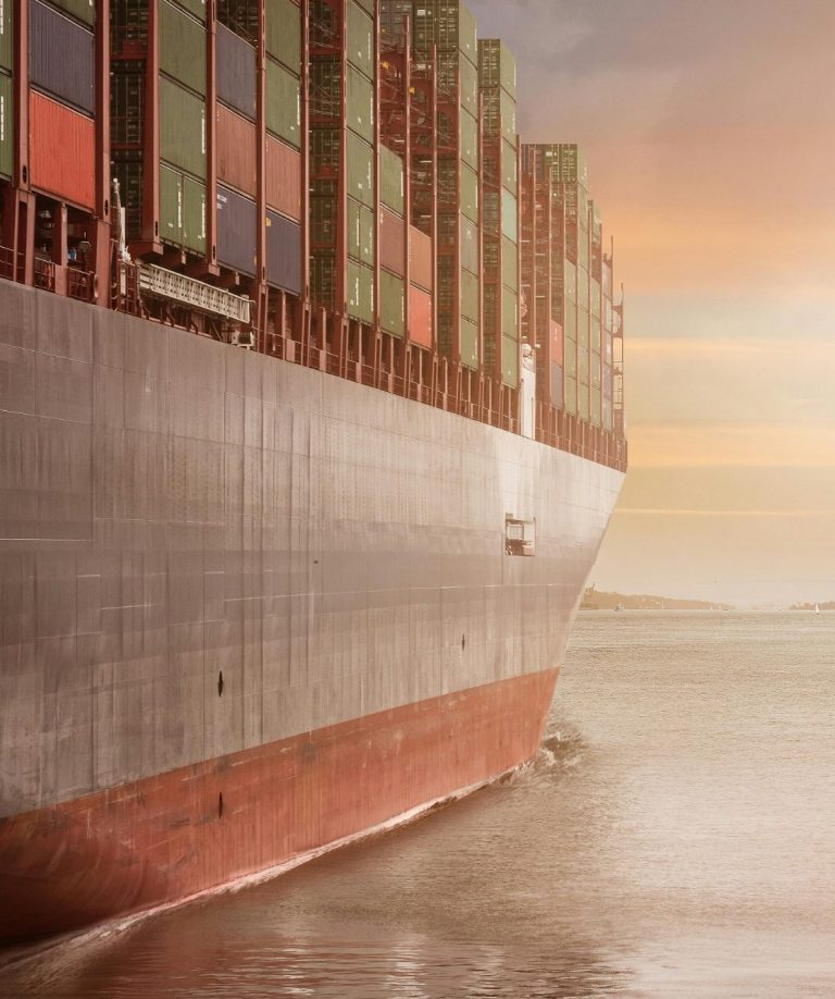 Container-Schiff fährt bei Sonnenuntergang durch ruhiges Wasser.