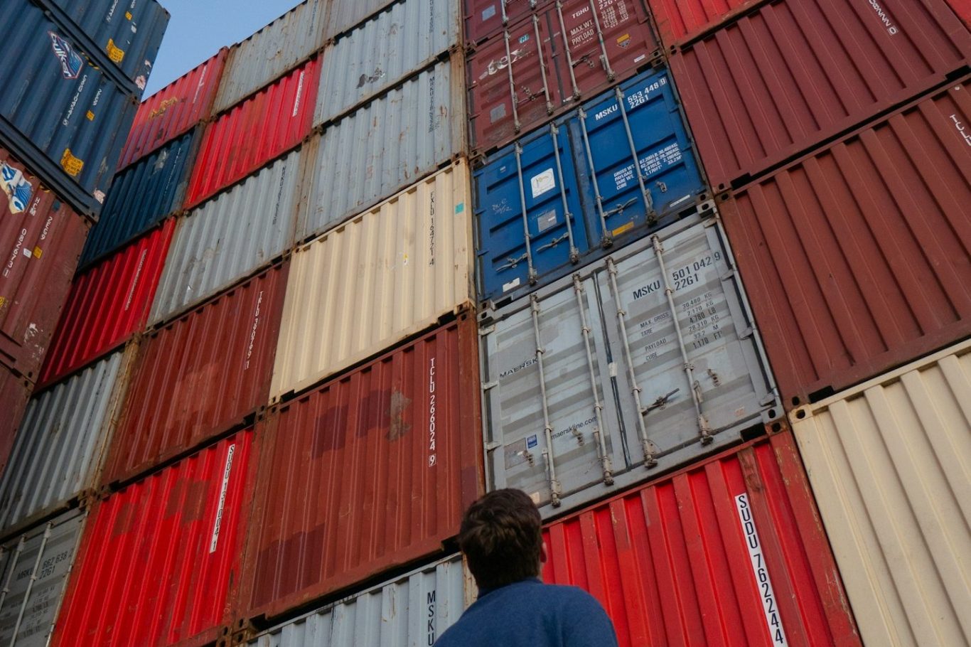Person betrachtet eine Wand aus farbigen Frachtcontainern.